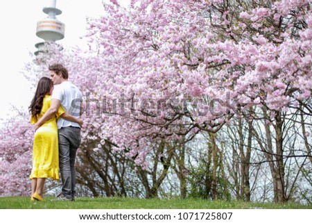 Man kissing woman with beautiful cherry blossom flower at park in Germany.Happy Mixed race asian-German couple hugging at beautiful Olympic Park in Munich city in spring to summer season.