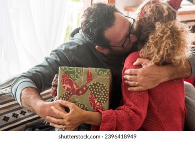 Man kissing woman at home and give her a christmas gift. Sharing xmas present concept leisure activity at home with real happy couple hugging with love and enjoyment. Love and relationship holiday - Shutterstock ID 2396418949