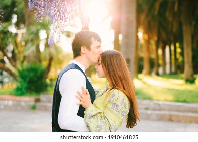 Man is kissing a woman on the forehead under a blooming wysteria tree in the park