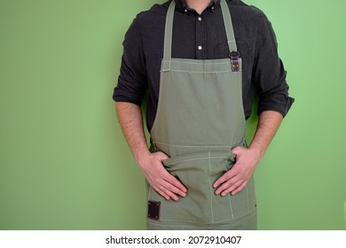 A man in a kitchen apron. Chef work in the cuisine. Cook in uniform, protection apparel. Job in food service. Professional culinary. Green fabric apron, casual stylish clothing. Handsome baker posing