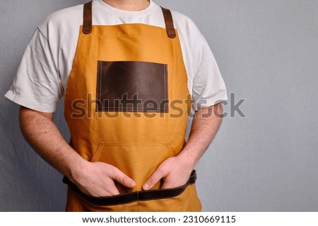 A man in a kitchen apron. Chef work in the cuisine. Cook in uniform, protection apparel. Job in food service. Professional culinary. Green fabric apron, casual stylish clothing. Handsome baker posing