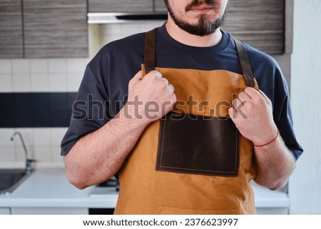 A man in a kitchen apron. Chef work in the cuisine. Cook in uniform, protection apparel. Job in food service. Professional culinary. Green fabric apron, casual stylish clothing. Handsome baker posing