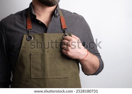 A man in a kitchen apron. Chef work in the cuisine. Cook in uniform, protection apparel. Job in food service. Professional culinary. Green fabric apron, casual stylish clothing. Handsome baker posing