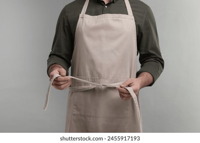 Man in kitchen apron on grey background, closeup. Mockup for design