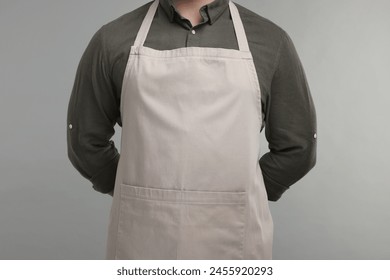 Man in kitchen apron on grey background, closeup. Mockup for design