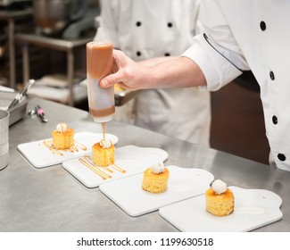 Man in a kitchen drizzling caramel sauce on small cakes topped with cream.