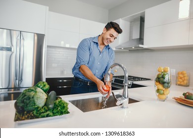 Man in a kitchen. A handsome man washes vegetables under water. Male at home with vagatables - Powered by Shutterstock