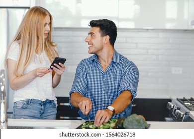 Man in a kitchen. A handsome man with woman at home. Male and famale at home with vagatables. Blonde with handsome guy prepare salad. Pretty girl use the phone near her boyfriend. - Powered by Shutterstock