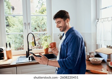 Man in kitchen having coffee while using his mobile phone