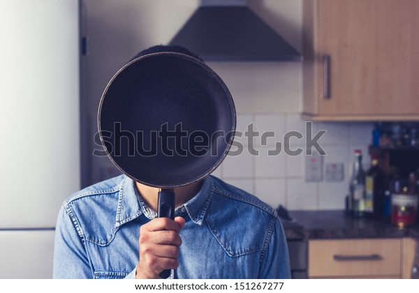 フライパンを顔の前に持つ台所の人 の写真素材 今すぐ編集
