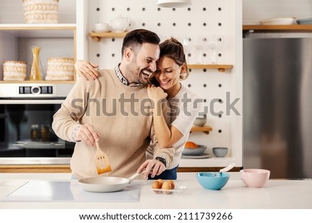 A man in the kitchen preparing a meal while his wife hugging him.