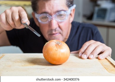 A Man In The Kitchen Tries To Cut An Onion Using Goggles To Avoid Tears, Shallow Depth Of Field With Focus On The Onion.