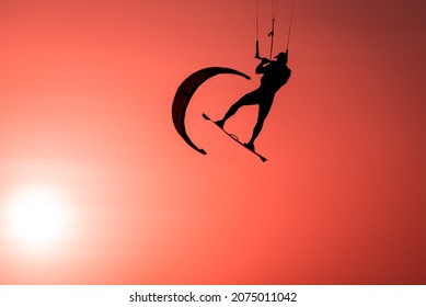 Man kiteboarder silhouette kiteboarder jumping sport at sunset golden hour, kite surfing athlete kiteboarding jump at kite surf