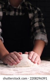 Man kneading dough at wooden table on dark background, closeup - Shutterstock ID 2208296391