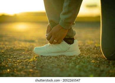 Man Kneeling Down Tying Shoes At Sunset