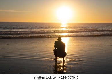 Man Kneeling On Beach At Sunset Over Ocean