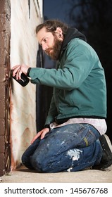 Man Kneeling On The Ground While Spray Painting A Wall