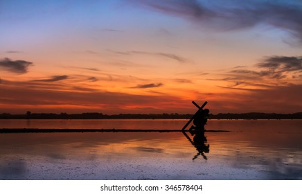 Man kneeling in prayer with a cross on his back, as the sunsets