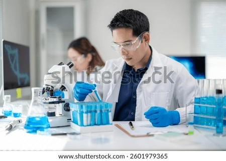 A man in a lab coat is working with a microscope. He is wearing a pair of blue gloves