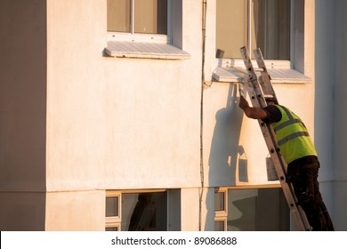 A Man Up A Ladder Painting The Exterior Of A House