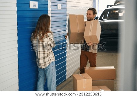 Man and lady with big cardboard boxes into warehouse with self storage unit