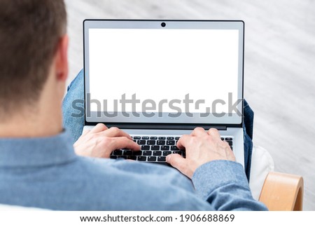 Man with laptop computer on lap working from home or in office with blank screen