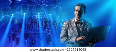 Man with laptop. Lighting equipment for concerts. Rack with spotlights. Man sets up lighting equipment. Guy controls spotlights through laptop. Concert equipment sales manager. Spotlights in dark