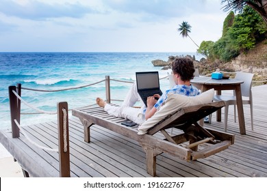 man with laptop and mobile phone running remotely on colorful beach of island, among the palms cafe.