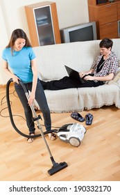 Man  With Laptop  Resting Over Sofa While Girl Doing House Cleaning With Vaccuum Cleaner