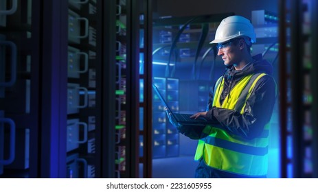 Man with laptop in server room. System administrator for industrial companies. Guy with computer. Server racks emit neon light. Maintenance industrial server equipment. Man in helmet in data center - Powered by Shutterstock
