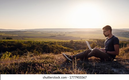 Mann mit Laptop sitzend am Rande eines Berges mit atemberaubendem Blick auf das Tal. Konzept der mobilen Netzabdeckung. 5G.