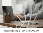 Man with laptop working at wooden table indoors, focus of Wi-Fi router