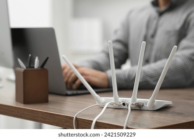 Man with laptop working at wooden table indoors, focus of Wi-Fi router