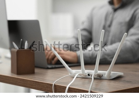 Man with laptop working at wooden table indoors, focus of Wi-Fi router