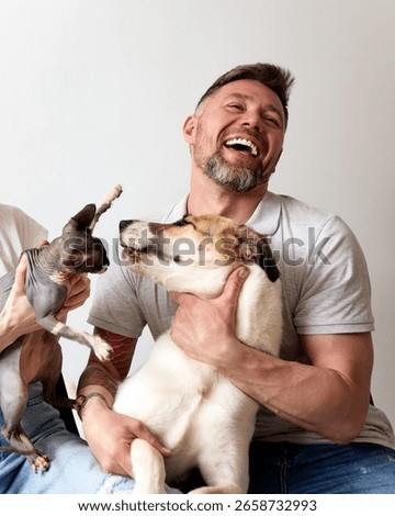 Man laughing while posing with a playful dog and a hairless cat