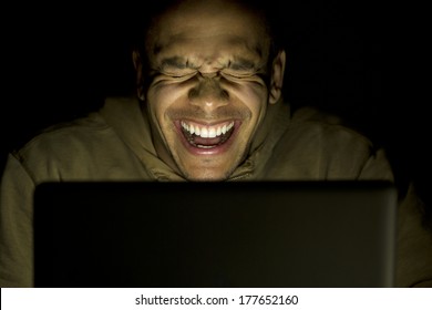 A man laughing whilst using his laptop at night, concept of modern technology use