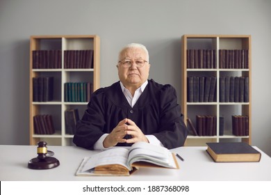 Man of law and justice. Honest wise mature male judge sitting at table in court. Portrait of serious fair incorruptible old lawyer at desk with gavel and open Code of Law in his office or courtroom