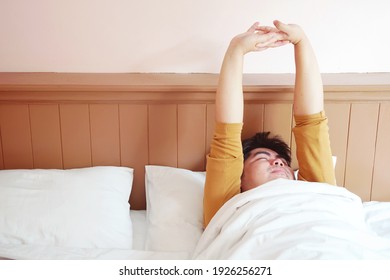 Man lay down on white bed, close eyes, stretching arms and lazy to awake in the morning.