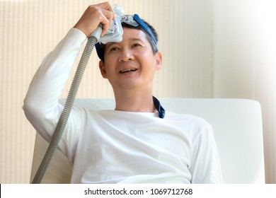 Man Laying In Bed Holding CPAP Mask With A Smiling Face After Waking Up From Daytime Sleepiness,front View Upper Body.Obstructive Sleep Apnea Therapy.