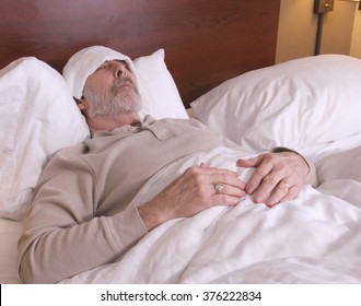 Man Laying In Bed With A Washcloth On His Head With A Fever And Chills