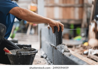 man is laying bricks in a wall. The bricks are black and the man is wearing a blue shirt - Powered by Shutterstock