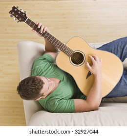 Man Laying On Couch Playing Guitar. Top View, Square Composition.