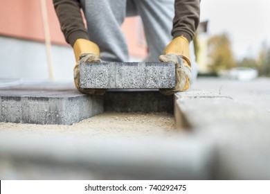 Man laying a paving brick placing it on the sand foundation in a low angle view.