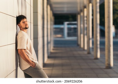 Man leaning on a facade while facing the camera outdoors during sunset
