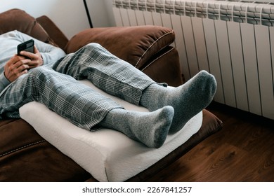 a man leans his legs on a leg elevation pillow, made of memory foam, while is resting on the sofa