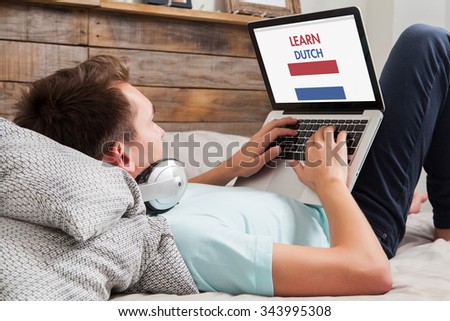 Man learning dutch language with a laptop computer lying down on the bed at home