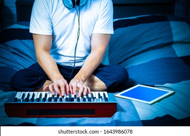 Man Learning Online Music Lesson And Playing Keyboard On Bed In Bedroom At Night