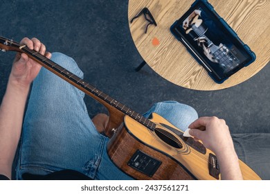 A man learns to play the guitar using a tablet, top view.