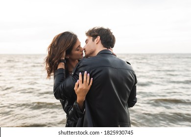 Man In Leather Jacket Kissing Girlfriend With Sea At Background