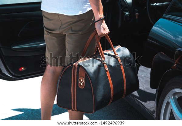 Man with with leather luggage bag\
standing near sports car. Luxury lifestyle\
concept.